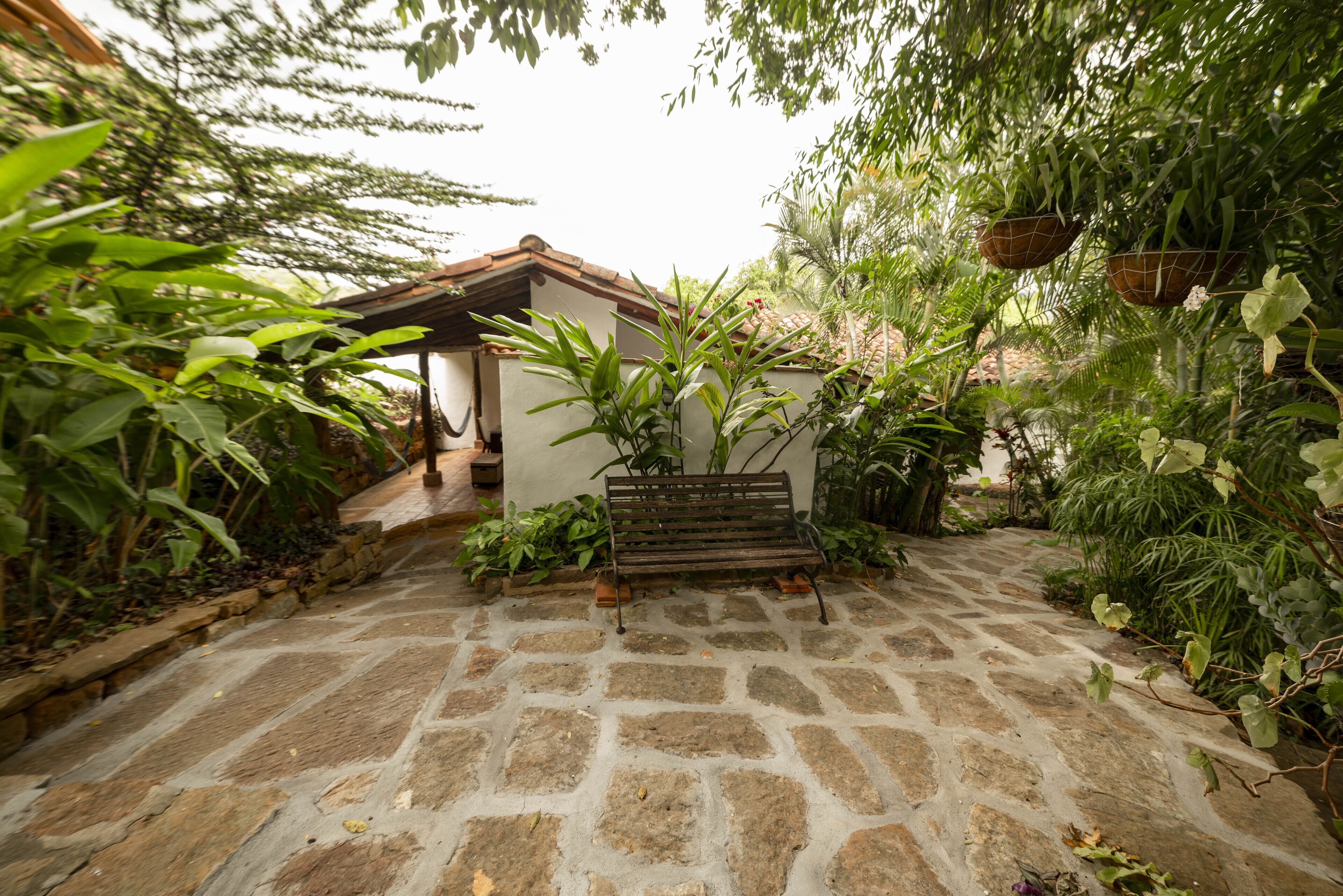 A stone-paved courtyard with a wooden bench and a white building with a tiled roof.