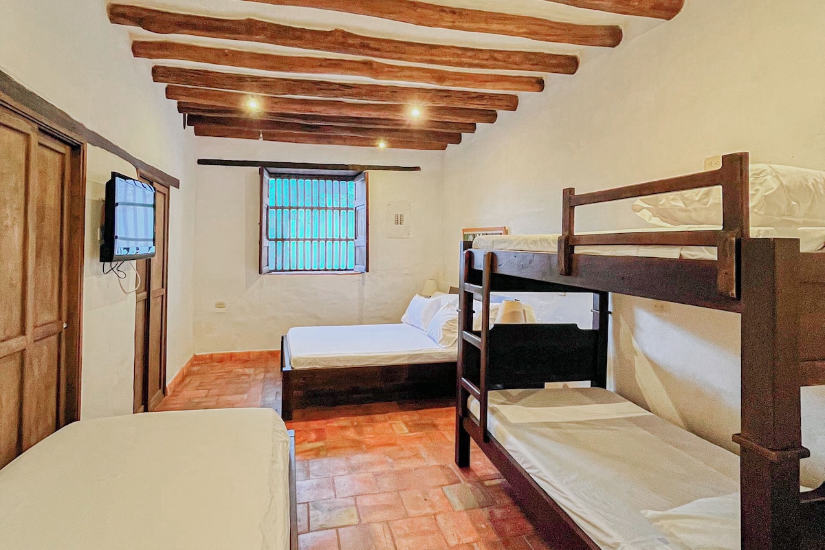 A room with bunk beds, a television, a window with bars, and wooden beams on the ceiling.