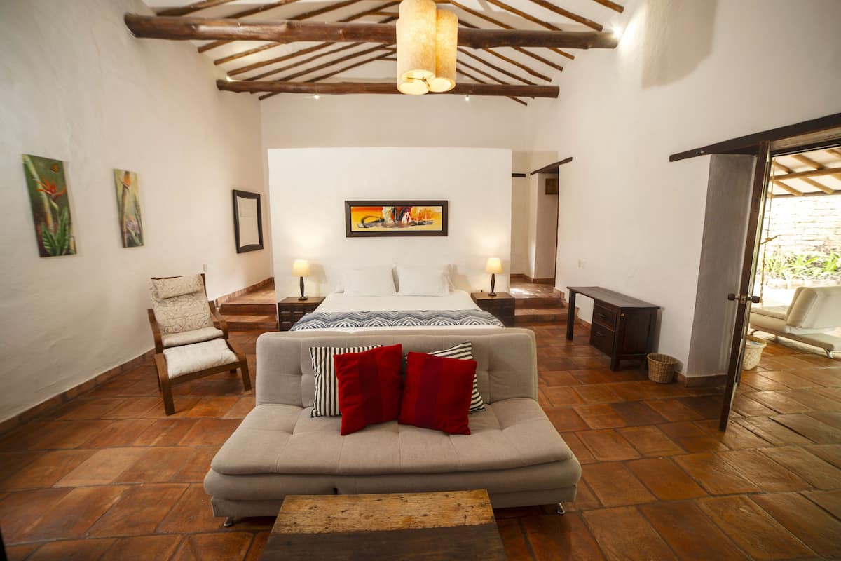 A spacious room with a sofa, a bed, and a dining table. There are paintings on the walls and a wooden ceiling.