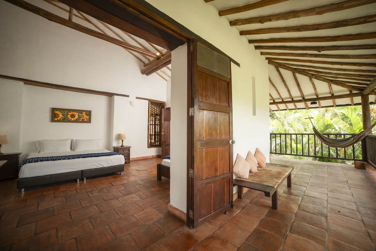 A bedroom with a bed, a wooden door, a bench, and a hammock.