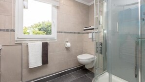 Ein modernes Badezimmer mit einer Glaskabine zur Dusche, einer Toilette und einem Fenster mit Tageslicht.