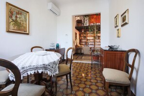 Uma área de refeições com uma mesa redonda, cadeiras, piso estampado e uma estante de livros ao fundo.