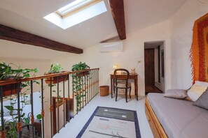 Quarto em estilo loft com claraboia, escrivaninha, cadeira, cama e plantas em vasos.