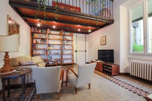 Uma sala de estar com um sofá, duas poltronas, uma televisão, uma estante de livros e um piso estampado.