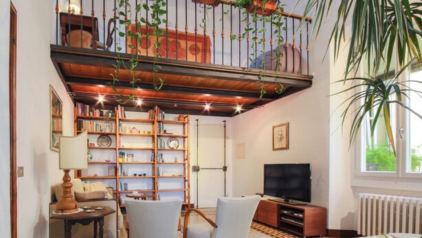 A living room with a bookshelf, two armchairs, a television, and a window with a view of greenery. - Apartments Florence- Sunny Via Romana (Firenze)