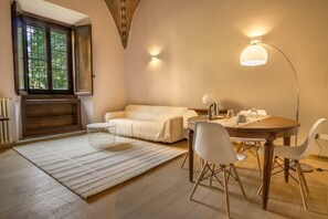 Una habitación acogedora con un sofá, una mesa de comedor con sillas, una lámpara y una ventana con vistas a árboles.