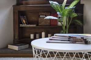 Ein Bücherregal mit Büchern und einer Topfpflanze, ein runder weißer Tisch und ein kleiner weißer Teppich.