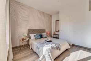 Een slaapkamer met een groot bed, een nachtkastje, een lamp, een spiegel en een deur.