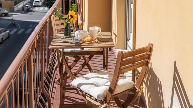 A balcony with a table set for two, a chair, a vase with sunflowers, and a view of the street. - Apartments Florence- Cherubini Balcony (Firenze)