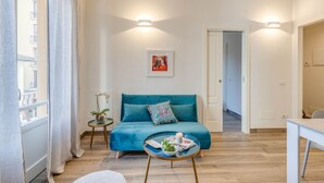 A living room with a teal sofa, a small round table with a candle, a framed picture on the wall, and a view through a window. - Apartments Florence- Cherubini Balcony (Firenze)