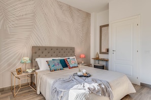 Een slaapkamer met een groot bed, een nachtkastje, een lamp, een spiegel en een deur.