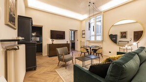 Ein Wohnzimmer mit Sofa, Couchtisch, Esstisch mit Stühlen, einer Küchenzeile und einem großen Spiegel.