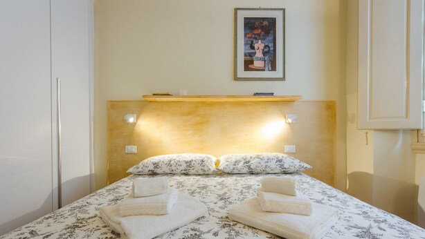 Ein Schlafzimmer mit einem Bett, Kissen, einem Kopfteil, einem Regal und einem gerahmten Bild an der Wand.