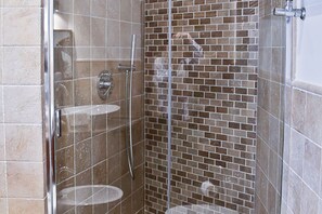 A shower with a glass door, a chrome faucet, and a tiled wall.