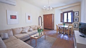 A living room with a sofa, coffee table, dining table, chairs, chandelier, and artwork on the walls.
