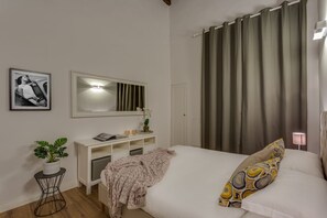 A bedroom with a bed, a bedside table, a mirror, a potted plant, and a wall-mounted light.