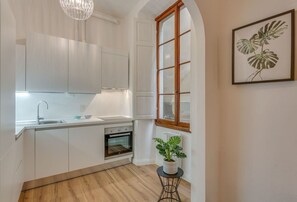 A modern kitchen with white cabinetry, a built-in oven, a sink, and a potted plant.