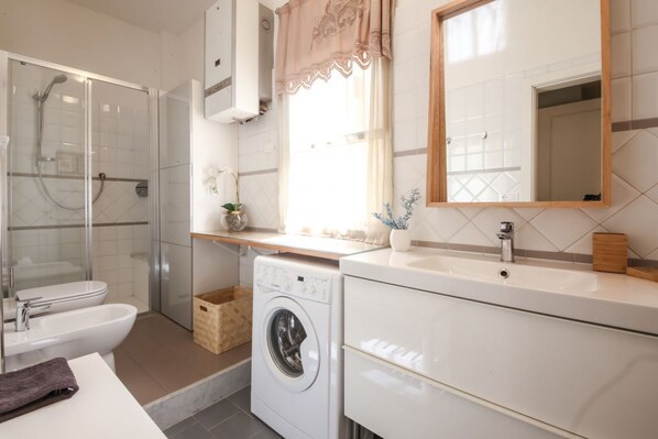 A modern bathroom with a glass shower enclosure, a washing machine, a sink, and a mirror. - Apartments Florence- San Martino (Firenze)