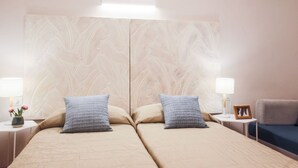 Une chambre d’hôtel avec un grand lit, deux tables de chevet, une commode, une lampe, un cadre photo et un canapé bleu.