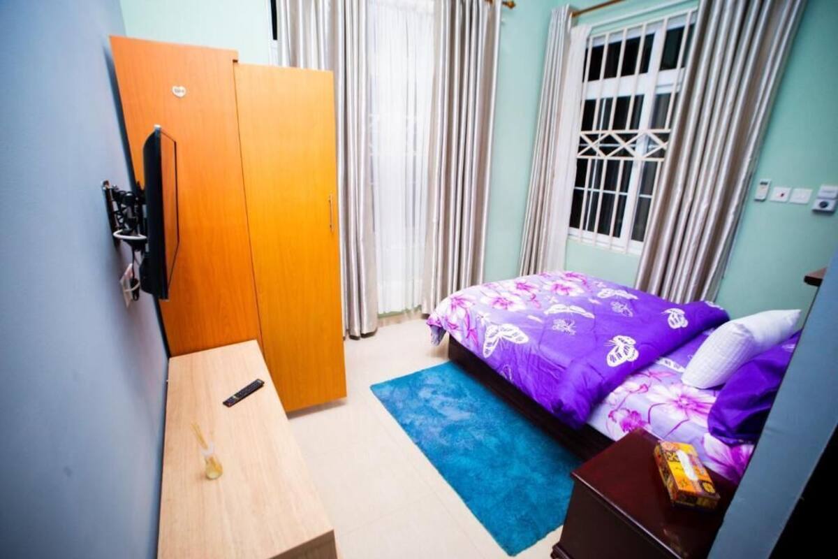 Ein Schlafzimmer mit Bett, Kleiderschrank, Schreibtisch und einem Fenster mit Vorhängen.