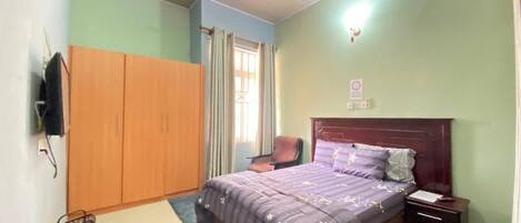 A bedroom with a bed, a nightstand, a chair, a wardrobe, a ceiling fan, and a window with curtains.