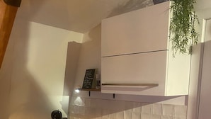 Una cucina compatta con lavandino, macchina del caffè e un piccolo vaso con una pianta sul piano di lavoro.