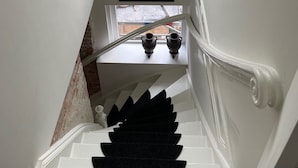Una scala con tappeto nero, un quadro incorniciato sul pianerotto e una finestra che dà sulla strada.