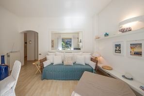 Un dormitorio con cama, una silla, una mesita, una estantería decorada y una ventana con cortinas.