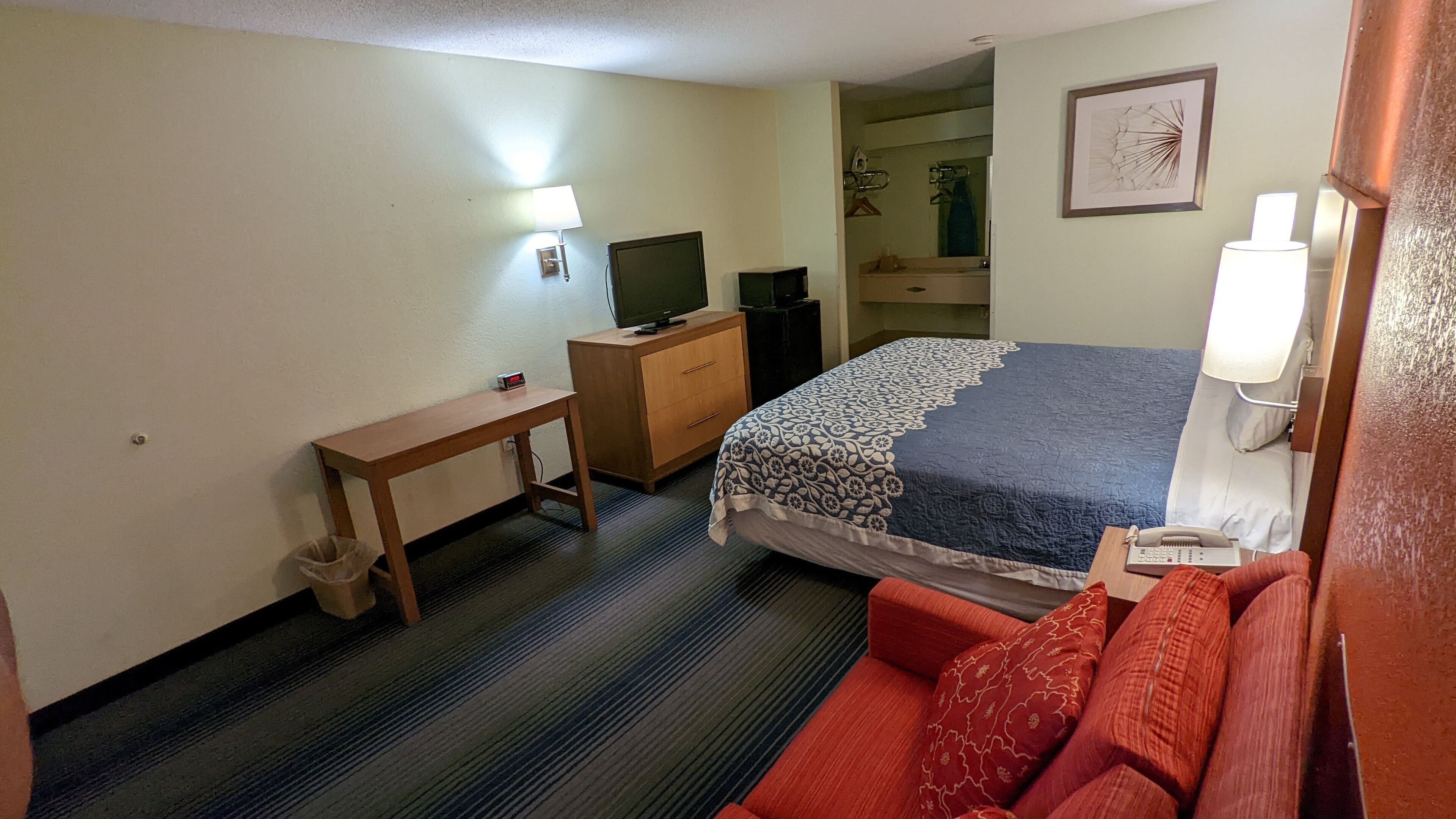 A hotel room with a bed, a desk, a television, a lamp, and a red sofa.