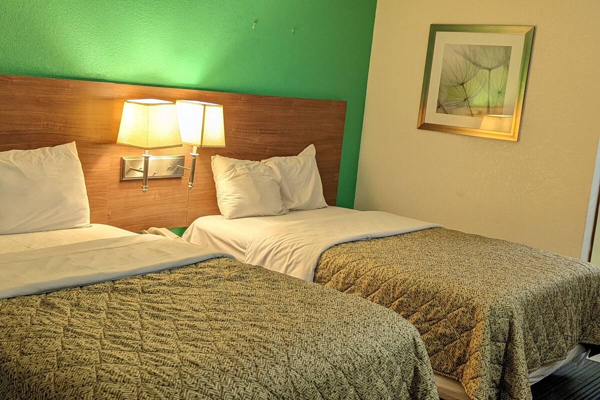 Habitación de hotel con dos camas, cabecero de madera, pared verde y un cuadro enmarcado.