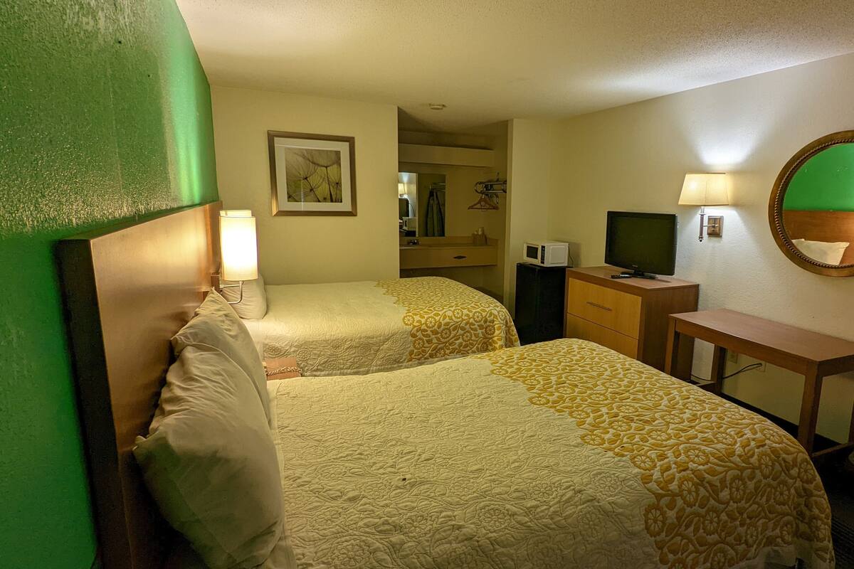Habitación de hotel con dos camas, un escritorio, televisor, espejo y un cuadro en la pared.