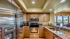 A modern kitchen with stainless steel appliances, wooden cabinets, granite countertops, and a view of the outdoors through large windows. - Waterfront condo with easy water access to world class fishing and sightseeing.  (Bokeelia)