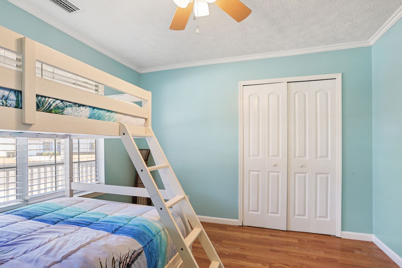 Una habitación con literas, una escalera, una puerta blanca y un ventilador de techo.