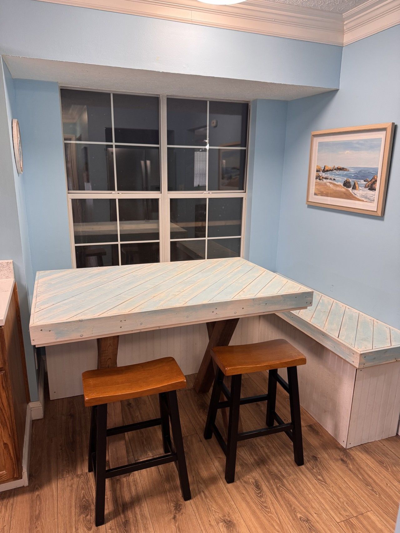 A dining area with a table and two stools, a window, and a framed picture on the wall.