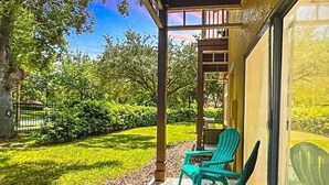 Un patio techado con dos sillas verdes, un camino de piedra y vistas a un exuberante jardín.