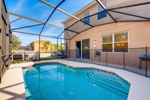 Une piscine dotée d’un espace couvert, un barbecue et une maison en arrière-plan.
