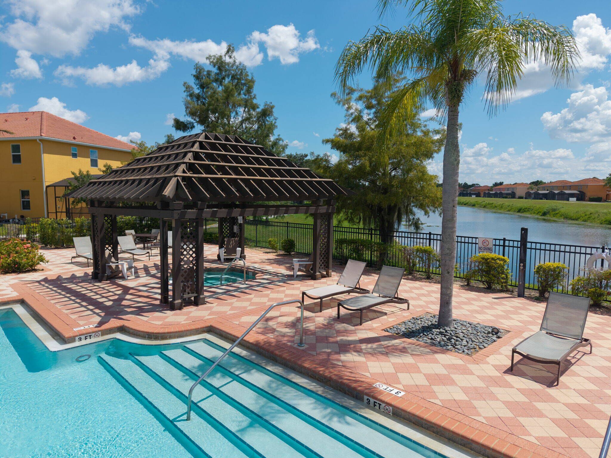 A pool area with lounge chairs, a pergola, and a view of a lake.