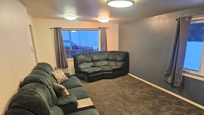 Ein Wohnzimmer mit einem Ecksofa, einem Liegesessel und einem Fenster mit Vorhängen.