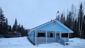 Ein blaues Gebäude mit Veranda und überdachter Auffahrt, umgeben von Schnee und Bäumen.