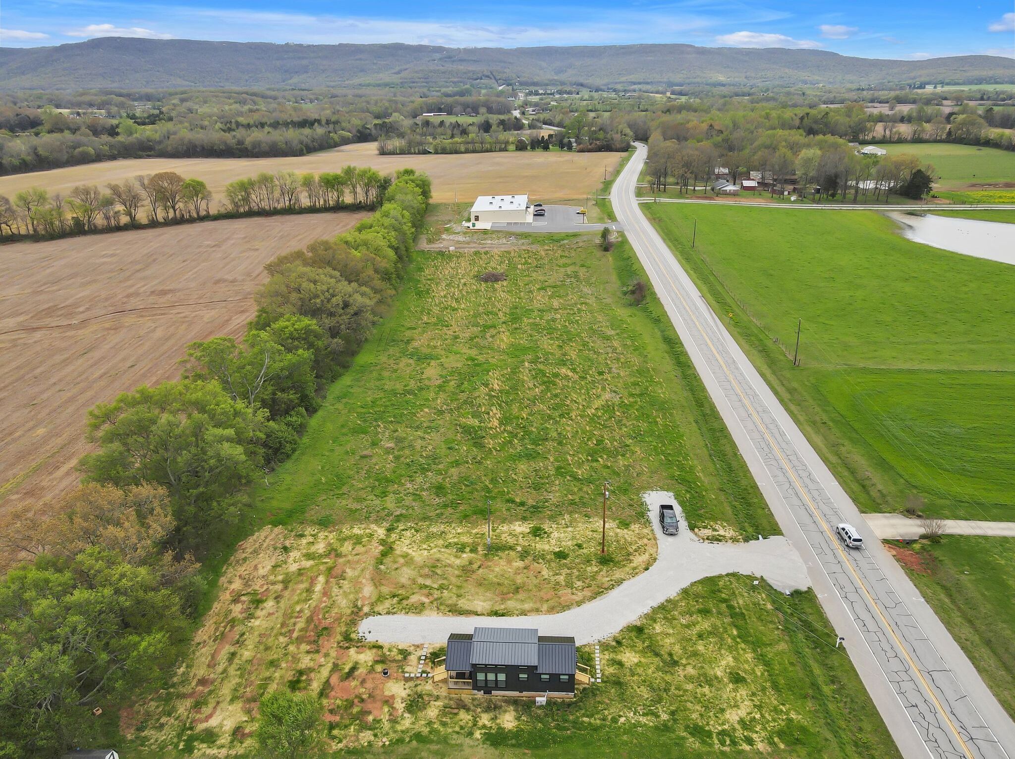 An aerial view of a rural property with a large field, a road, and a building with a dark roof.