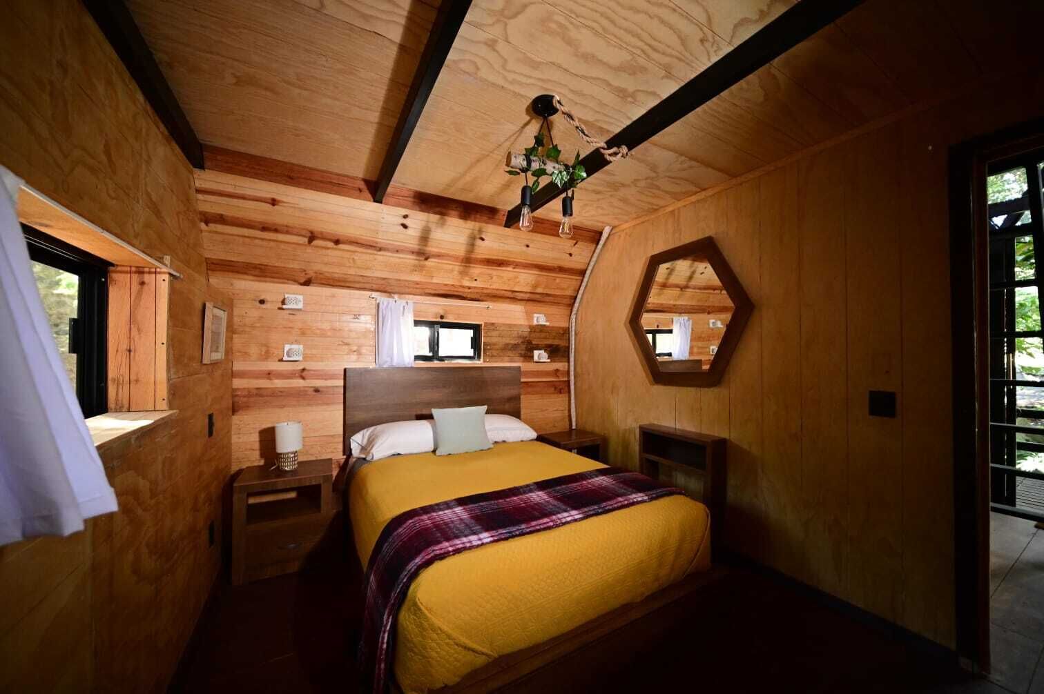 Quarto de cabana de madeira com cama, mesas de cabeceira, janela e espelho.