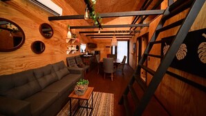 Un interior rústico de madera con sofá, mesa de comedor y sillas, una escalera con diseño de hojas y una lámpara colgante.