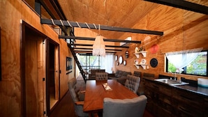 Una cocina moderna con detalles de madera, un comedor con una mesa grande y varias sillas, y vistas al exterior con vegetación.