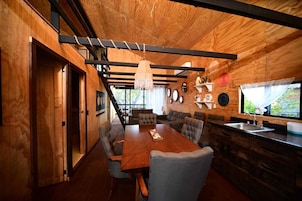 Una cocina moderna con detalles de madera, un comedor con una mesa grande y varias sillas, y vistas al exterior con vegetación.