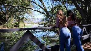 Dos personas de pie en una cubierta de madera con vistas a un cuerpo de agua y árboles al fondo.