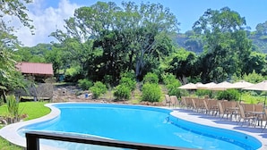 Una piscina con borde curvo, rodeada por una terraza con sillas y mesas.