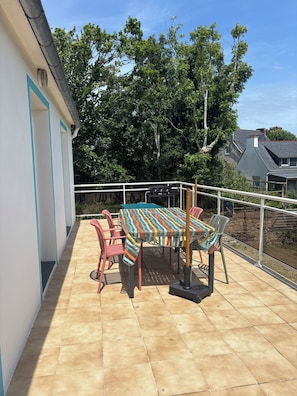 Un patio con una mesa, sillas, una parrilla y vistas a árboles y casas.