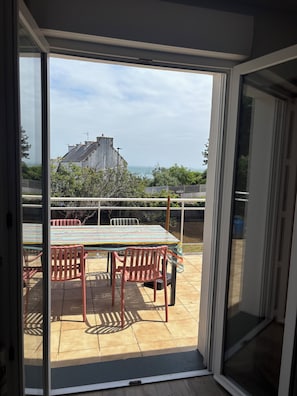 A balcony with a table and chairs, a view of the sea, and a building in the background.