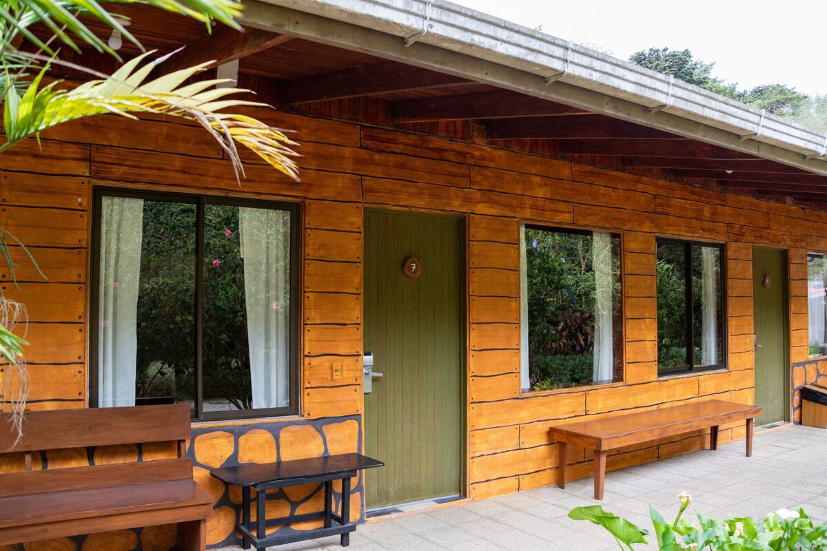 A wooden cabin with large windows, a green door, and outdoor seating.