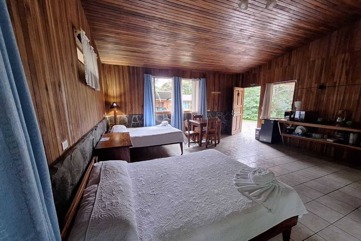 A wooden cabin with two beds, a dining table, and a kitchen area.